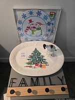 All four items displayed: packaged round snowman tray, oval Christmas tree platter, cow creamer, FAMILY wall hanger
