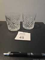 Two cut glass rock glasses on black surface