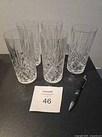Five clear cut highball glasses standing together beside a pen and lot tag