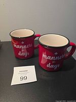 Front view of both red enamel mugs showing text and maple leaf