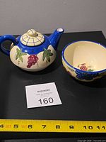 Teapot with lid and matching teacup side by side, measuring tape for scale