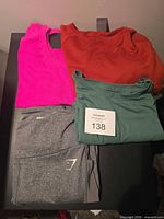All four garments folded: pink tank, rust top, green tee, gray Gymshark leggings