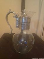 Full view left profile of carafe showing glass body and metal handle