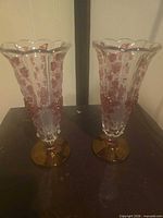 Full view of both vases showing clear glass, pink floral motif, amber bases