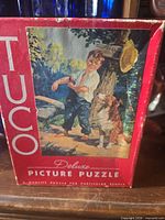 Front of red Tuco Deluxe Picture Puzzle box showing illustration of boy with dog
