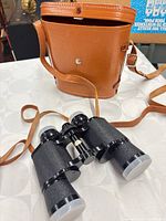 binoculars with lens caps beside brown carrying case