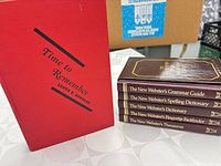 Five books; red Time to Remember standing, four stacked Webster's guides