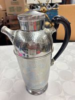 Front view of hammered chrome cocktail shaker with black Bakelite handle and caps attached