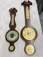 Both wooden banjo-style weather stations side by side