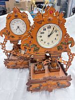 Full view of both carved wood wall clocks on white background
