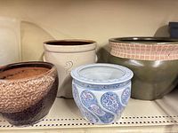 Front view shows four vessels on shelf: brown planter, stoneware crock, green planter, blue/white planter