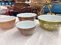 Four bowls displayed: two Woodland Brown pattern bowls (caramel tan, dark brown) and one Spring Blossom Green pattern bowl alongside all items for scale