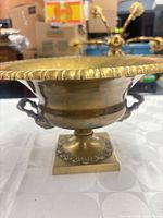 Side view of brass pedestal bowl showing ribbed rim, body, handles, and square base