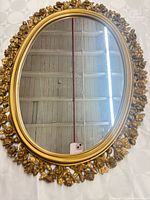 Full front view of oval mirror showing gold floral frame and glass