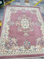 Full view of the rose-colored wool area rug showing entire design and fringe