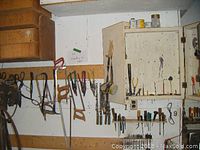 Photo of wall-mounted white tool cabinet with tools hung around including saws, pliers, screwdrivers