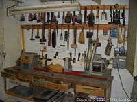 Wide view of workbench with lathe/machinery and multiple hanging tools including brushes and hammers