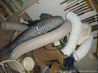 Dust collector unit with hoses and bag in workshop setting.