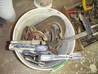 Top view showing a white bucket filled with large metal C clamps and bar clamps, some with wooden handles.