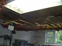 Multiple pipe clamps hanging from ceiling-mounted wooden rack