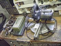 Electric miter saw with attached sliding arm, green and black metal toolboxes, group of seven steel C-clamps on wooden workbench