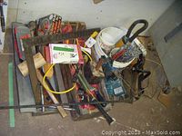 Photo showing assortment of tools including cordless drill, wooden mallets, large metal square, and buckets with hand tools.