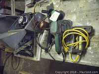 Multiple power tools seen on a workbench including sander, grinder, router, and staple gun cord