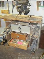 Front view of the Craftsman radial arm saw mounted on the wooden workstation, showing the wooden drawers open with various small items inside and wooden dowels stored on the side compartments.