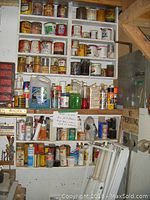 Wide view of shelves with assorted paint cans, automotive fluids, and cleaning supplies