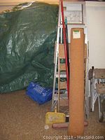 Roll of cork material standing upright beside two step ladders and three brooms.
