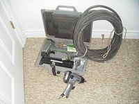 Air power nailer in opened carrying case, air impact wrench, and coiled air hose arranged on floor.