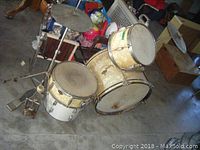Overview of the kids drum set including bass drum, two tom-toms, snare drum, cymbals and foot pedals placed on concrete floor.