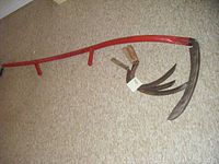 Photo showing the entire vintage scythe with red handle and three handheld scythes on floor.