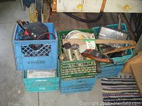 Six plastic milk crates stacked with various tools and accessories including socket sets, work lights, saws, and axes.