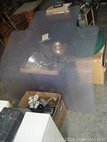 Large clear textured plastic computer chair mat on floor with assorted items around it.