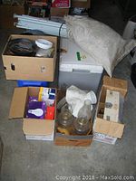 Wide shot showing multiple items: white gazebo frame poles, powered cooler, canvas sack, cardboard boxes with camping and lighting items