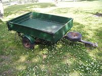 Side view of green small utility trailer parked on grass, showing overall condition and size.