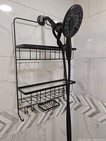 Front view of black metal shower caddy hung over showerhead showing three tiers and hooks