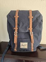 Front view of navy Herschel backpack showing brown buckle straps and logo patch