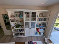 Front view of three connected white IKEA LIATORP shelving units showing two open bookcases flanking a glass-door cabinet