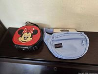 Front view of Minnie Mouse red vinyl handbag and JanSport light blue waist pack