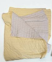 Full view of yellow quilted throw folded to show striped reverse