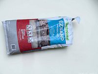Bag of Techniseal EZSand polymeric sand 35 lb grey, label and slit-open corner visible
