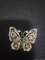 Front view showing filigree wings, rhinestones, green cabochon body