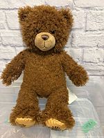 Front view of brown Build-A-Bear Harry Potter collaboration bear showing gold paw pads with Hogwarts crest embroidery.