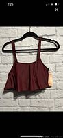 Front view of burgundy ruffle bikini top on hanger with tag visible