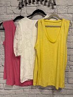 Front view of three women’s tops: pink sleeveless, white puff-sleeve floral, yellow sleeveless