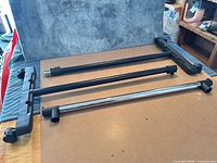 Disassembled chrome horizontal bar and two black plastic caster bases with black telescoping uprights on tabletop