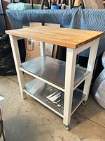 Full view of kitchen cart showing butcher block top, stainless shelves, white frame, casters