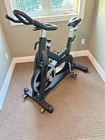 Full view of HMC Trainer 5008 exercise bike showing frame, flywheel, handlebars, pedals and transport wheels